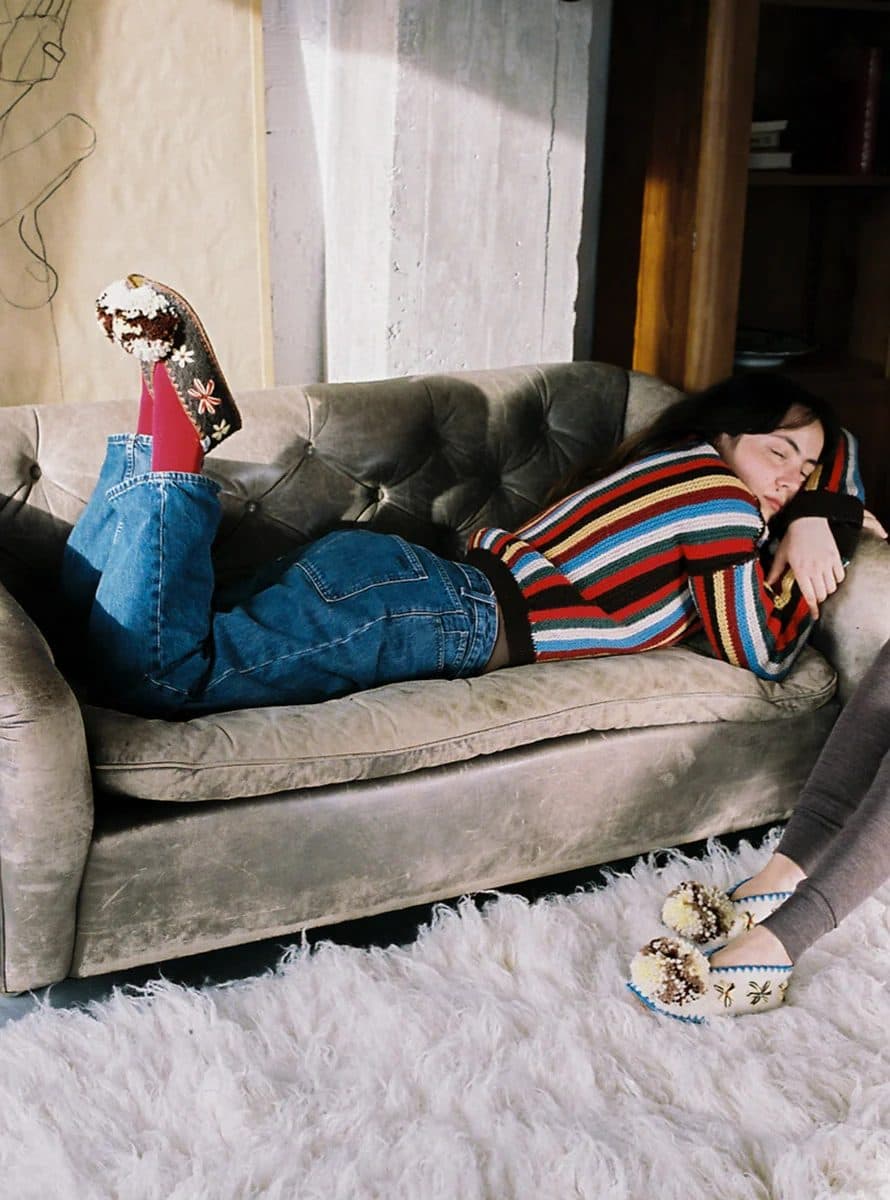 A woman asleep on a leather sofa wearing Give A Pon pompom slippers