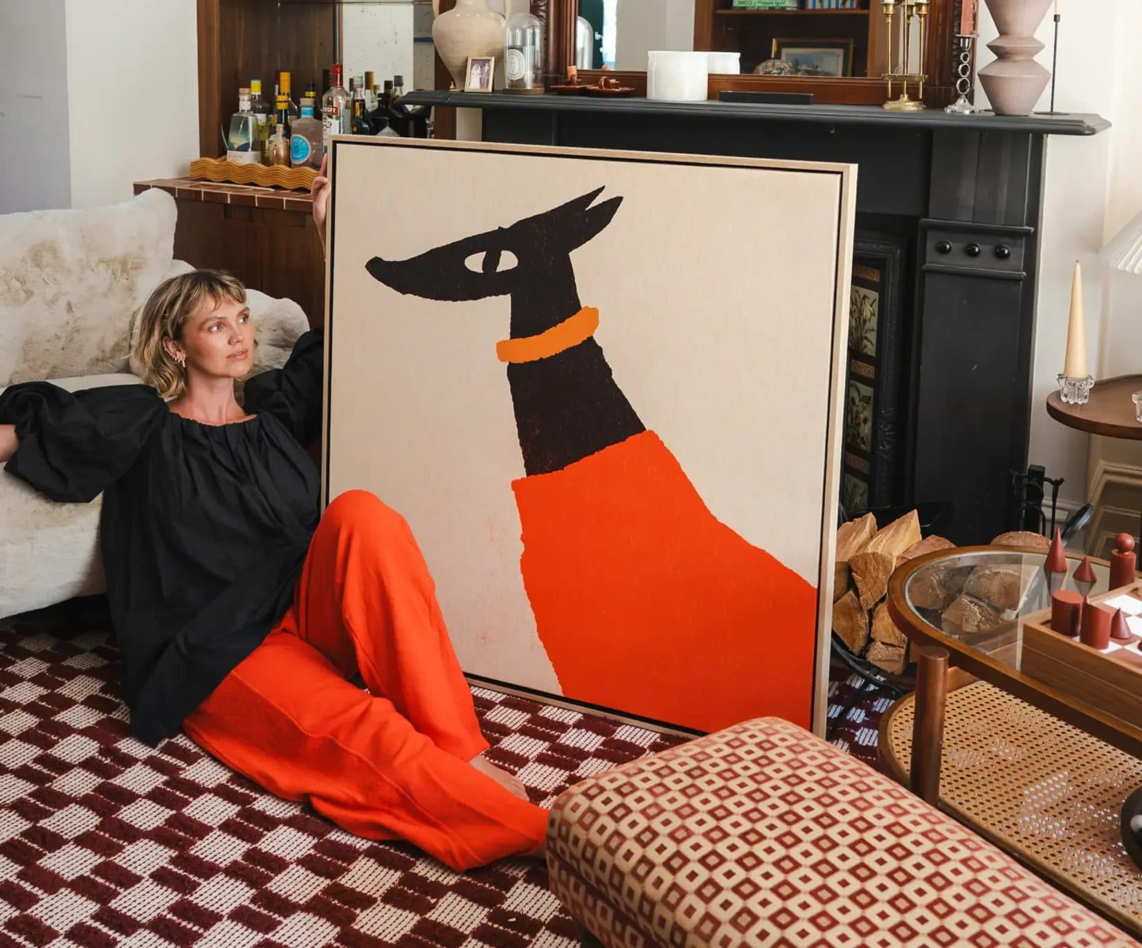 A woman sitting on a rug next to a large framed print of a black and orange dog