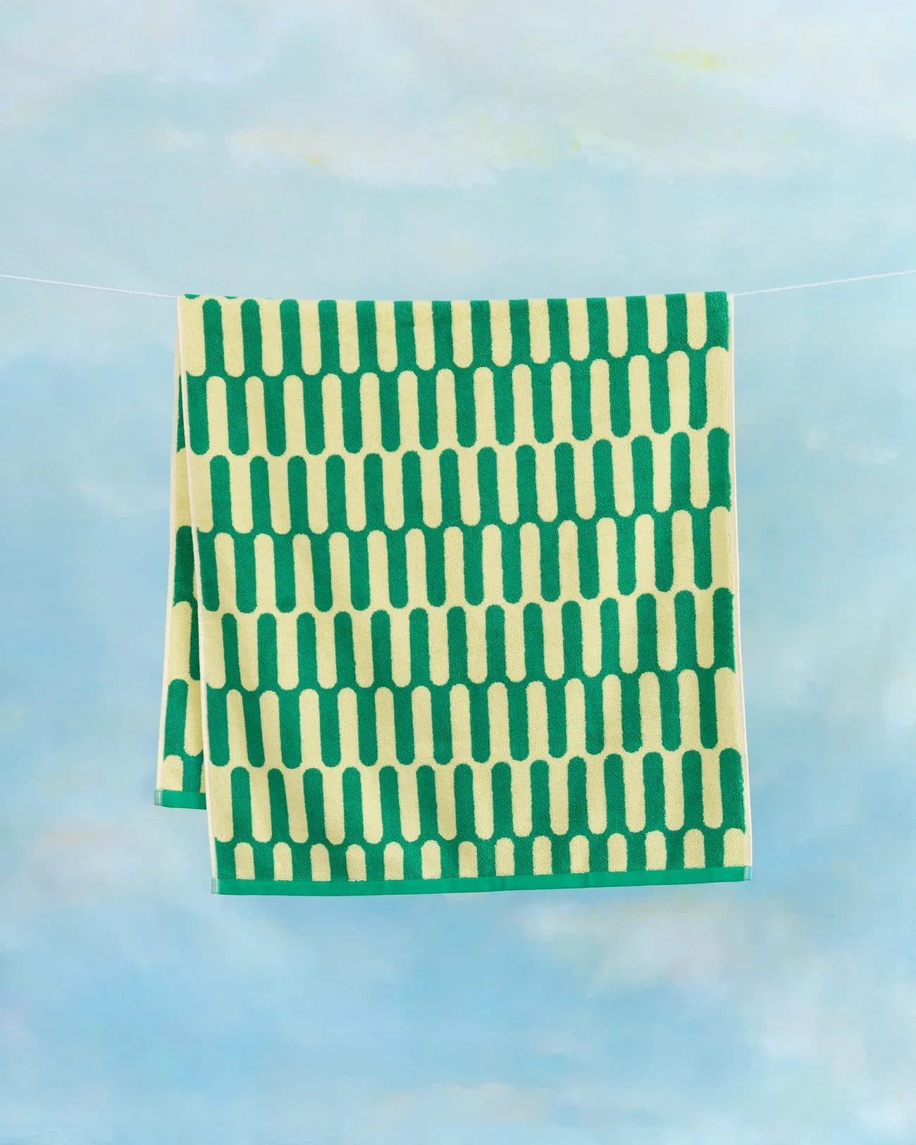 A green and cream patterned Tarta Gelatina towel on a washing line against the sky