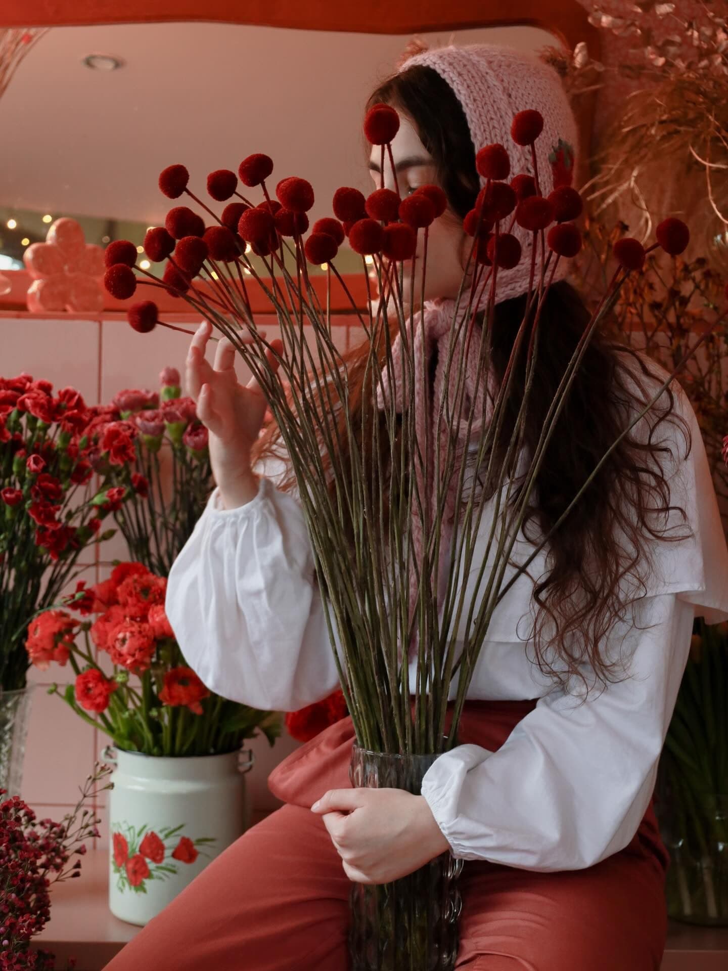 A woman in a pink knitted headscarf behind a bouquet of red craspedia